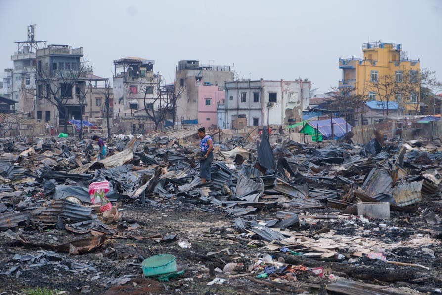 A woman collects scrap metal on a trash heap in Mandalay, Myanmar, that caught fire during the 2025 earthquake.