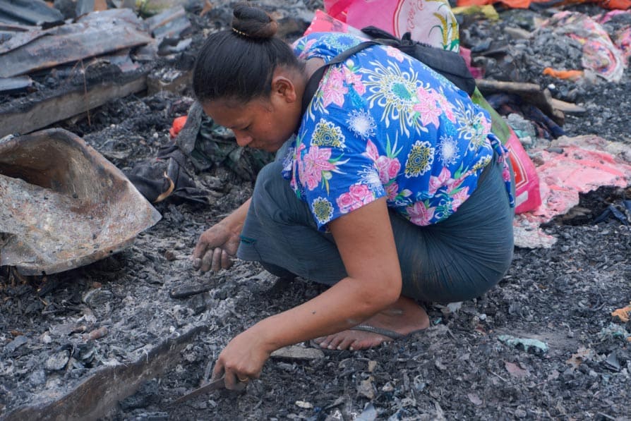 A woman collects scrap metal on a trash heap in Mandalay, Myanmar, that caught fire during the 2025 earthquake.