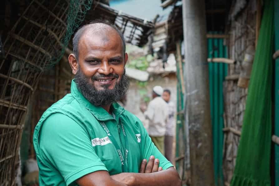 A man stands with folded arms looking at the camera in Kutupalong Refugee Camp, Bangladesh.