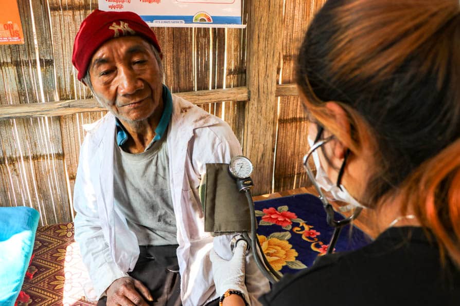 A health worker uses a stethoscope and blood pressure cuff while conducting a health check of an elderly man at a community clinic in rural Myanmar.