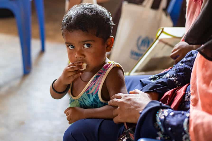 A young child eats while standing between his mother's legs in Kutupalong Refugee Camp, Bangladesh.