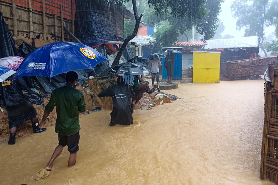 People holding umbrellas wade through floods and heavy rain in Kutupalong Refugee Camp, Bangladesh.
