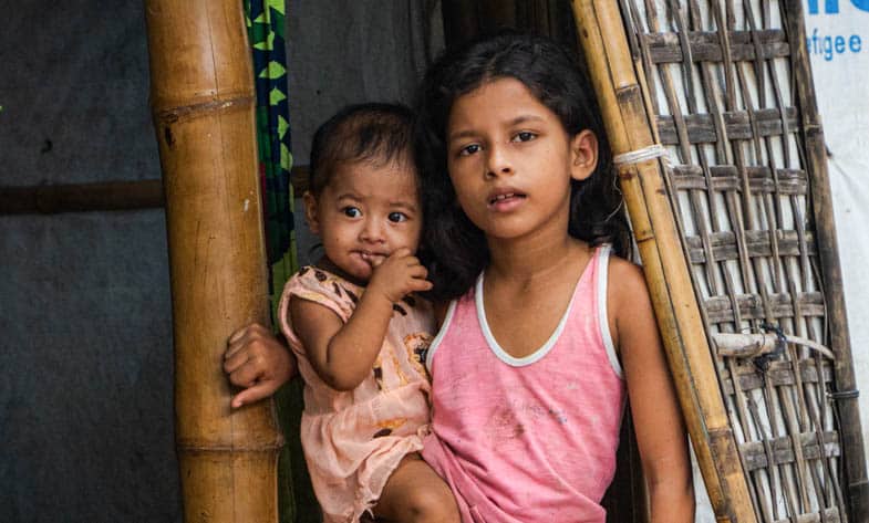 A Rohingya child holds her baby sister in the doorway of a shelter in Kutupalong Refugee Camp, Bangladesh.