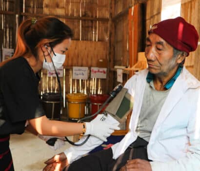 A health worker in a community clinic in Myanmar uses a blood pressure cuff to check the blood pressure of an elderly patient.
