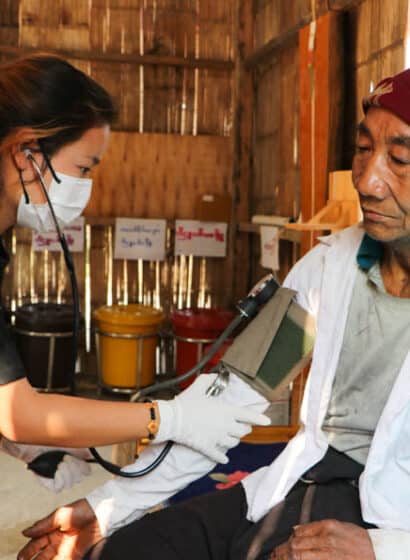 A health worker in a community clinic in Myanmar uses a blood pressure cuff to check the blood pressure of an elderly patient.
