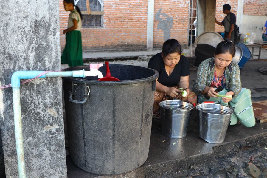 Two women peel vegetables as part of community meal preparation at a school in southeastern Myanmar.