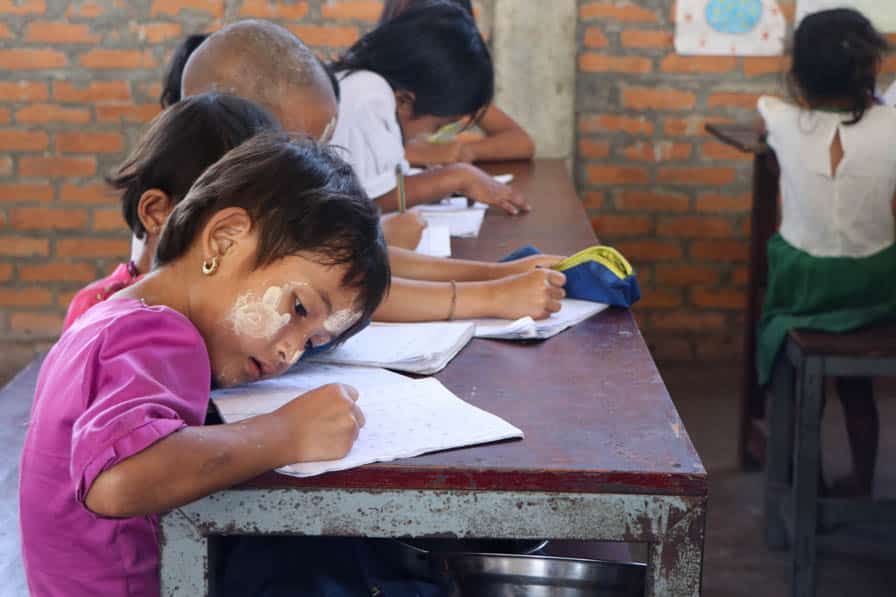 Children sit writing at a desk at a school in southeastern Myanmar.