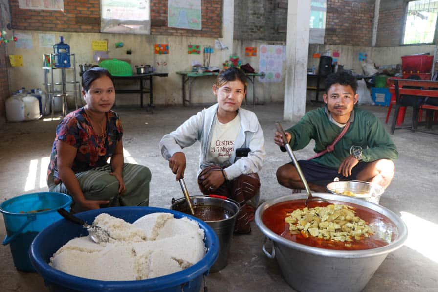 Community members sit with food prepared for children at a school in southeastern Myanmar