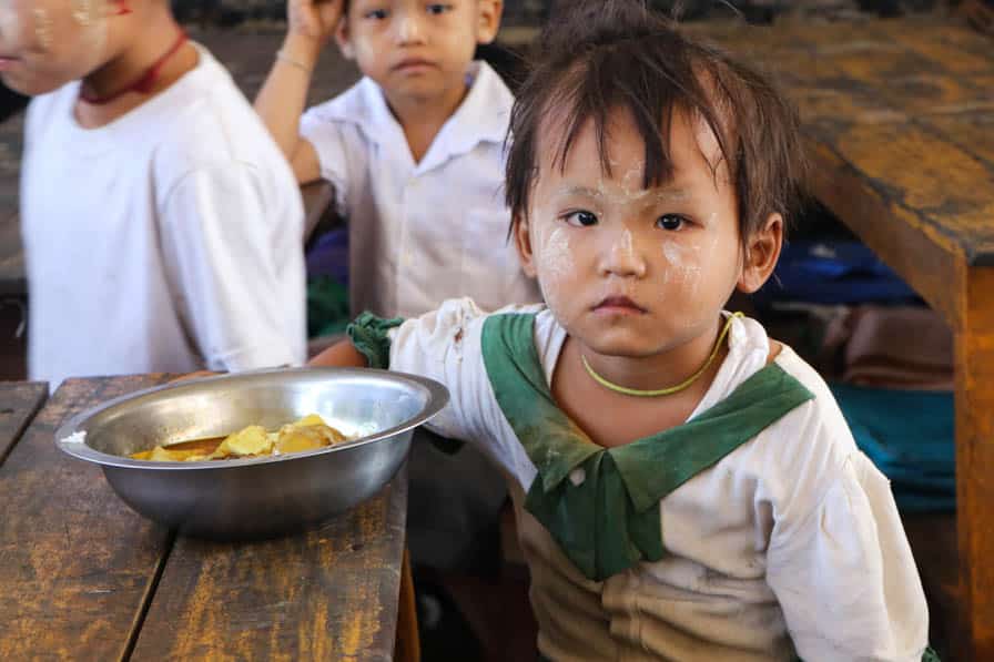 A young girls sits a a desk with a plate of food prepared by community members at her school in southeastern Myamar.
