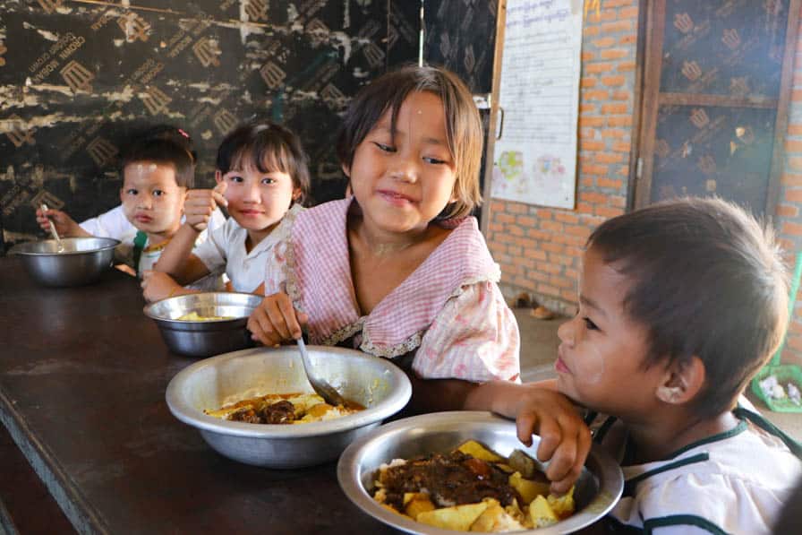 Children sit at a table at their school in southeastern Myanmar eating a meal prepared by community members.