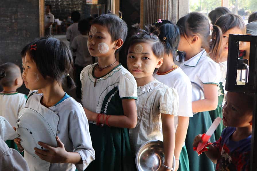 Children holding bowls queue for a meal at a school in southeastern Myanmar.
