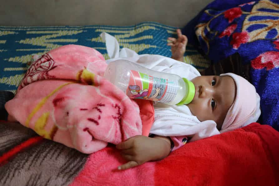 A baby lies on a bed with a bottle in its mouth at a maternity waiting home in southeastern Myanmar.