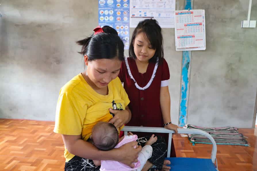 A woman breastfeed a baby while her young daughter looks on at a maternity waiting home in southeastern Myanmar.