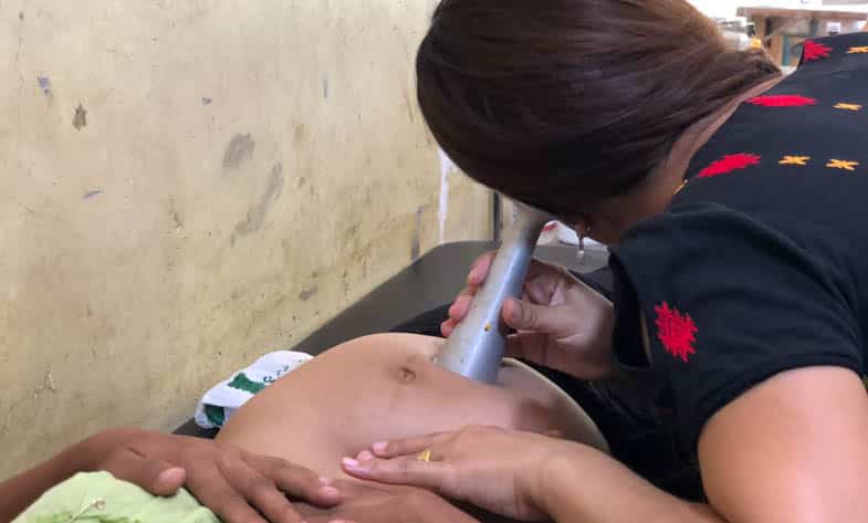 A health worker in Myanmar uses a Pinard horn to listen to a baby's heartbeat.