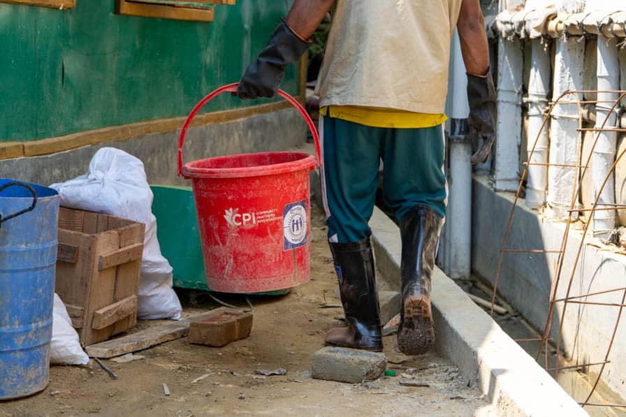A Rohingya WASH worker carries a bucket while making concrete cesspit rings in Kutupalong Refugee Camp, Bangladesh.