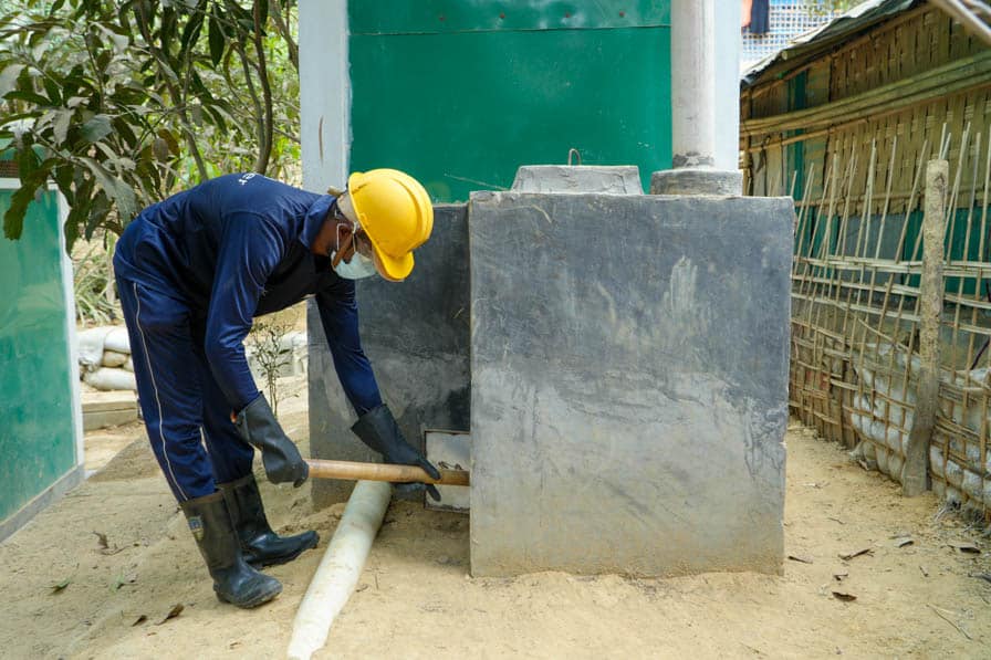 A Rohingya sanitation worker clears out ash from the incinerator of a menstrual hygiene management chamber attached to a toilet block in Kutupalong Refugee Camp, Bangladesh.