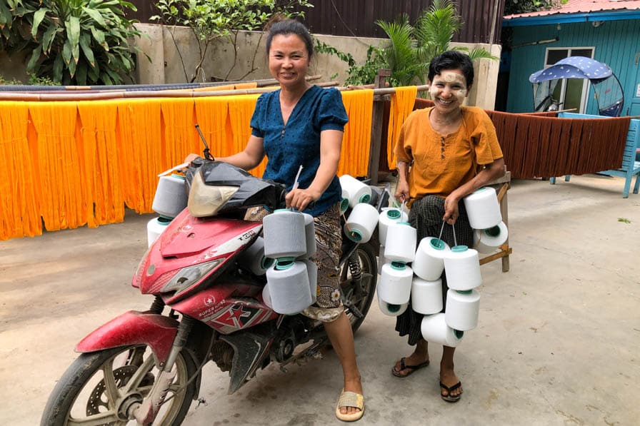 Two women, holding many spools of yarn, stand by a motorcycle in Amarapura, Myanmar.