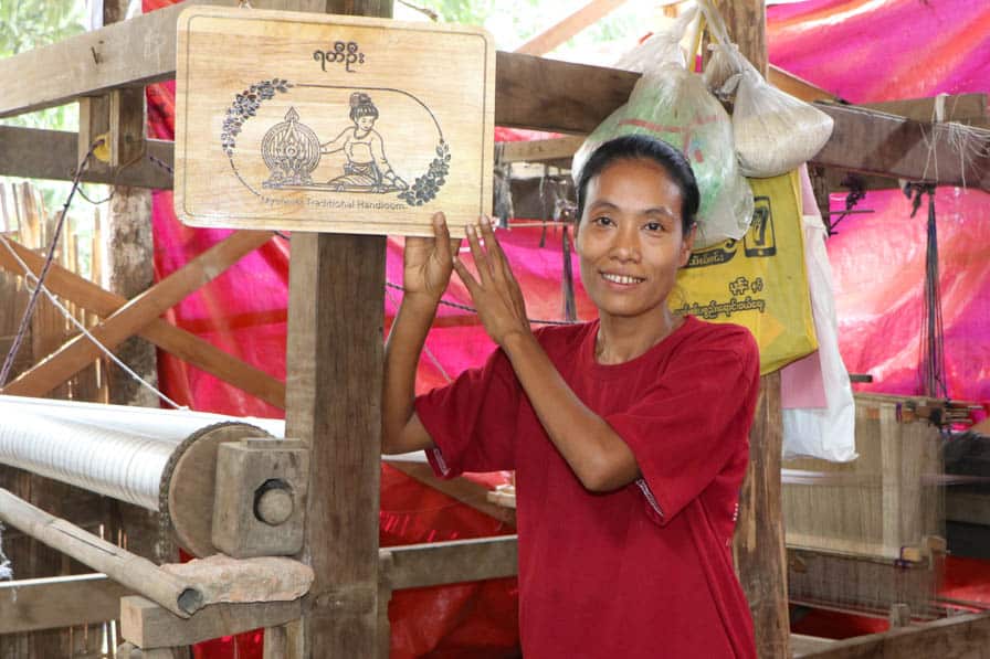 Ma Marloo Oo holds up a signboard with the name of her weaving shop "Yatty Oo" in her handloom workshop in Amarapura, Myanmar.