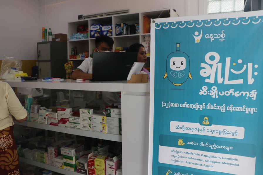 An advertisement for NCD care stands beside the pharmacy at Nae Thit Kyan Mar's clinic in Amarapura, Myanmar.