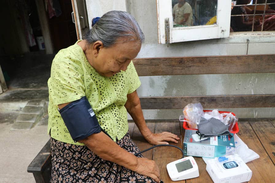 Daw May checks her blood pressure at home in Amarapura, Myanmar, using a monitor supplied through Nae Thit Kyan Mar's NCD care subscription package.